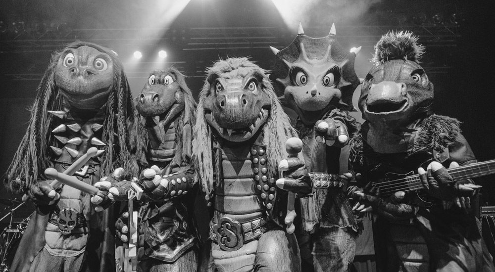Photo en noir et blanc du groupe Heavysaurus qui propose du metal pour les enfants avec des artistes déguisés en dinosaures